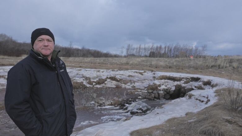 a man stands on a marsh in front of an aboiteau which is part of a dyke. 