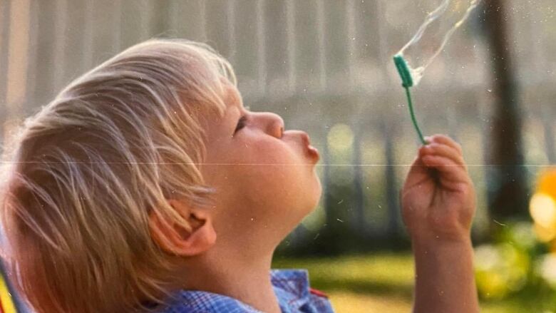 A blond-haired boy blows a bubble in a 1980s-era colour film photograph.