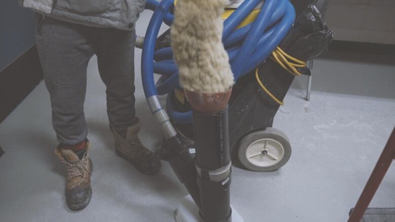 A man holds a ceiling duster to a vacuum tube in the ground.