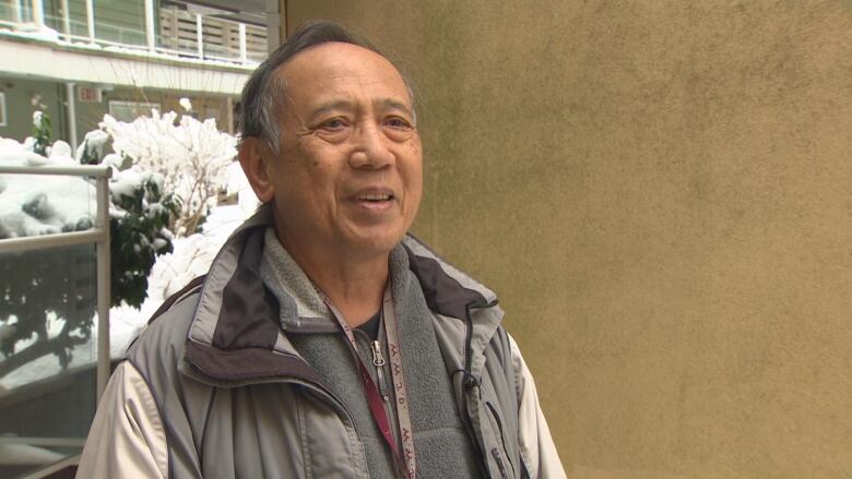 An older East Asian man is pictured outside with snowy conditions behind him.