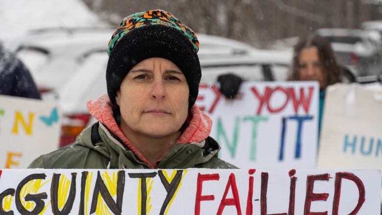 Women in a winter hat, holding a protest sign looks directly into the camera