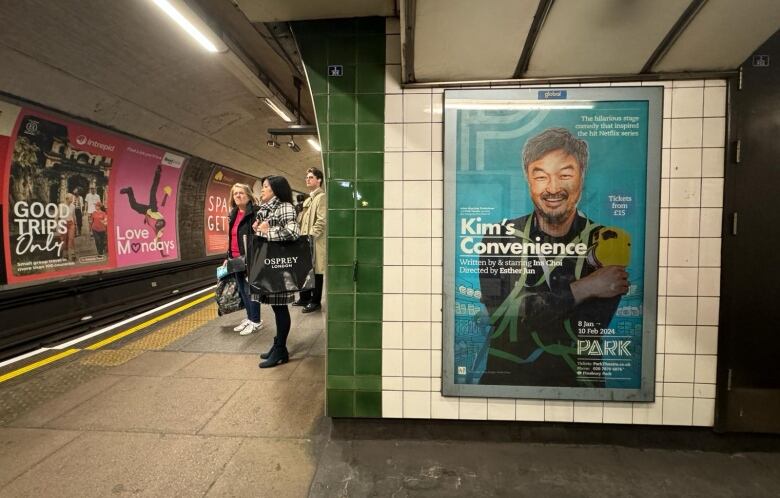 People stand on a subway platform adorned with posters.