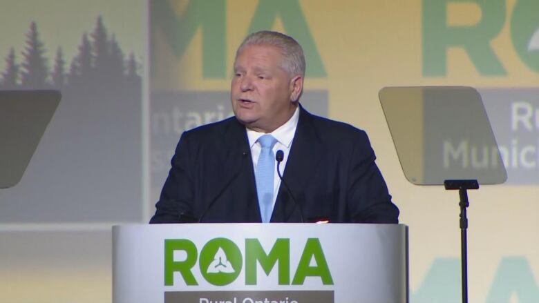 A man in a suit speaks on stage in front of a podium.