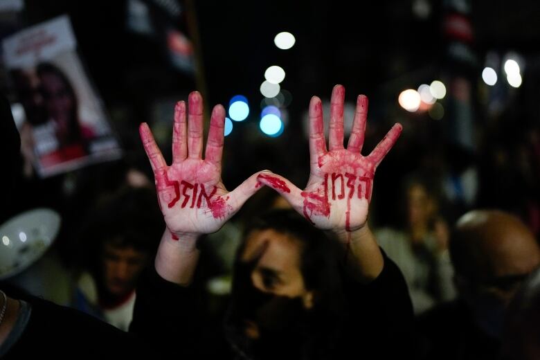 A woman in a crowd of people holds up her hands with Hebrew letters written on her palms in bright red fake blood.