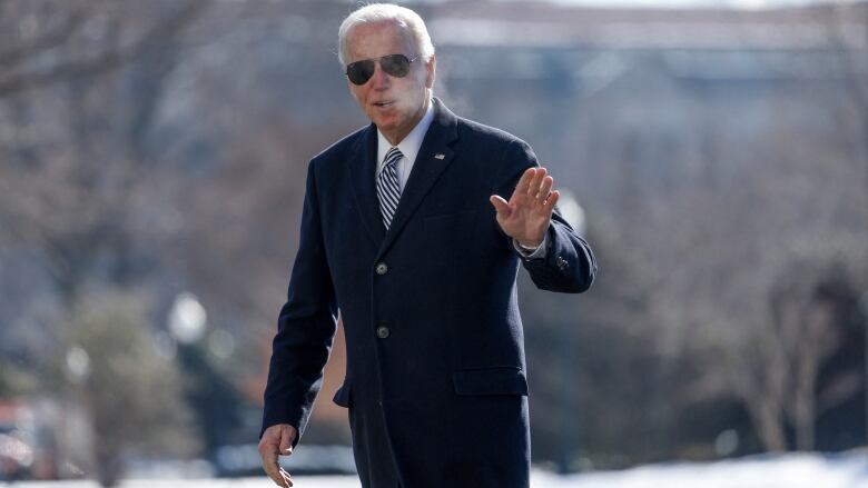 Biden in long winter coat and aviator glasses, waves from a snowy White House lawn with vapor rising from his breath into cold air  