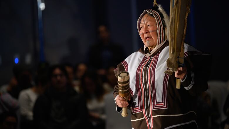 a woman in a white and brown parka dances and sings on stage