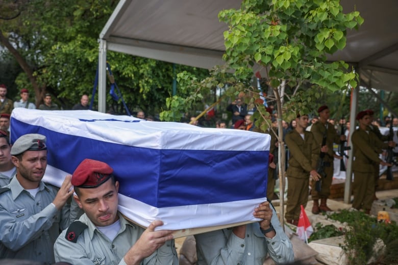 Three men are shown carrying a coffin draped in the Israel flag on their shoulders.