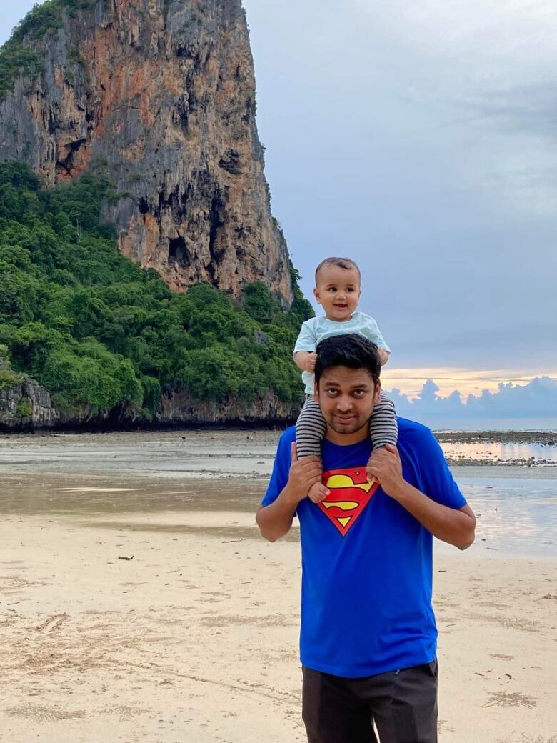 A young man has his baby on his shoulder, posing with the mountain in their background.