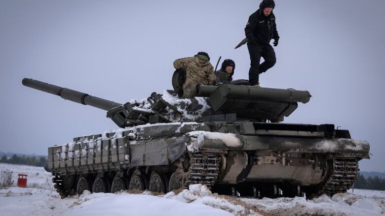 Three soldiers stand on top of a tank.