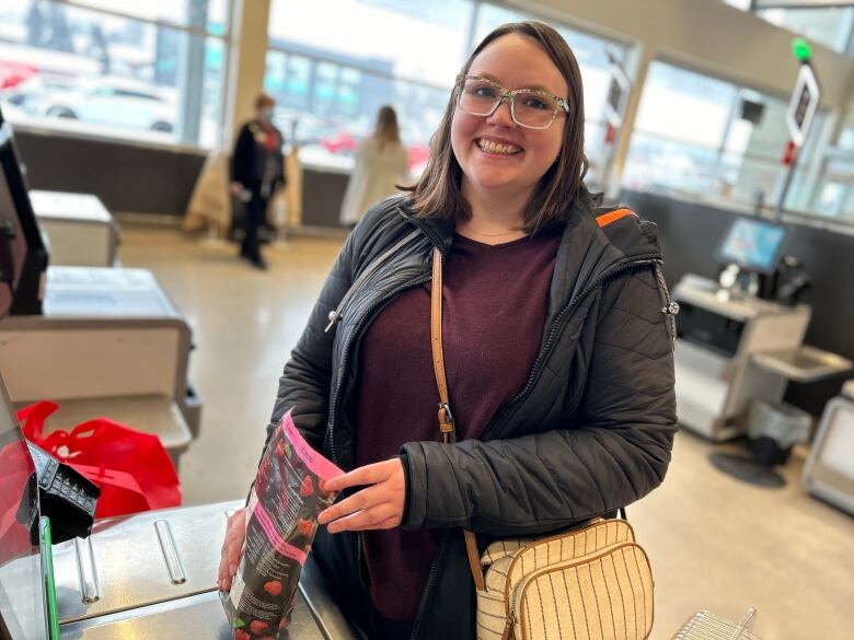 A woman smiles for a photo at a grocery store's self-checkout kiosk.