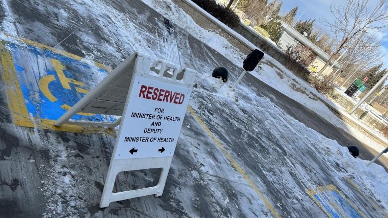 a white sign is placed in a snowy parking lot over top of accessible parking spaces. the sign reads 