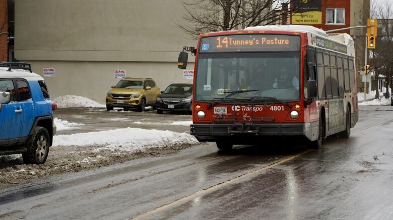 An OC Transpo bus drives down the street. The sidewalks are snowy. 