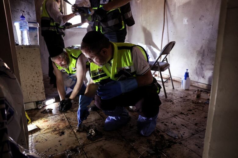 Men in high-viz vests collect evidence from the floor of a damaged house.