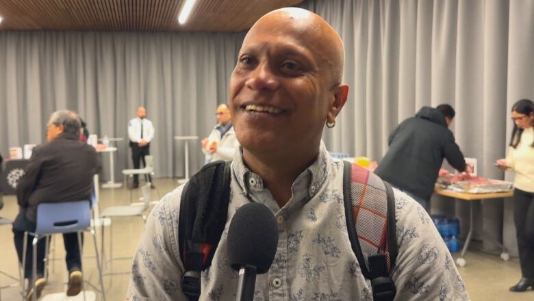 A man wearing a backpack smiles at the camera.