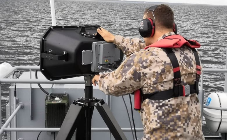 A high-powered speaker is aimed seaward by a soldier from the deck of a boat. 