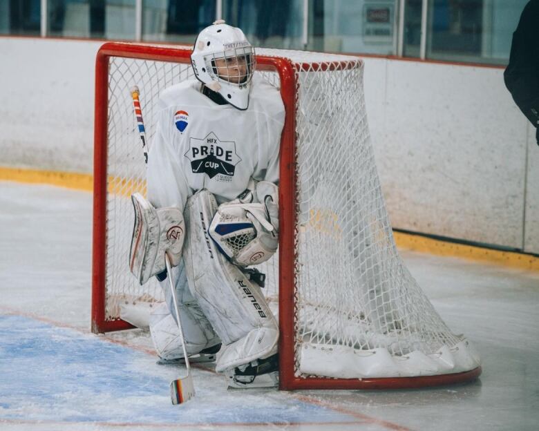 Person wearing hockey gear, stands in front of a goalie net in a ice rink. 