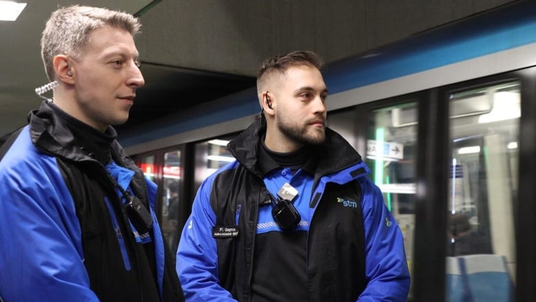 Two men stand in front of a metro train.