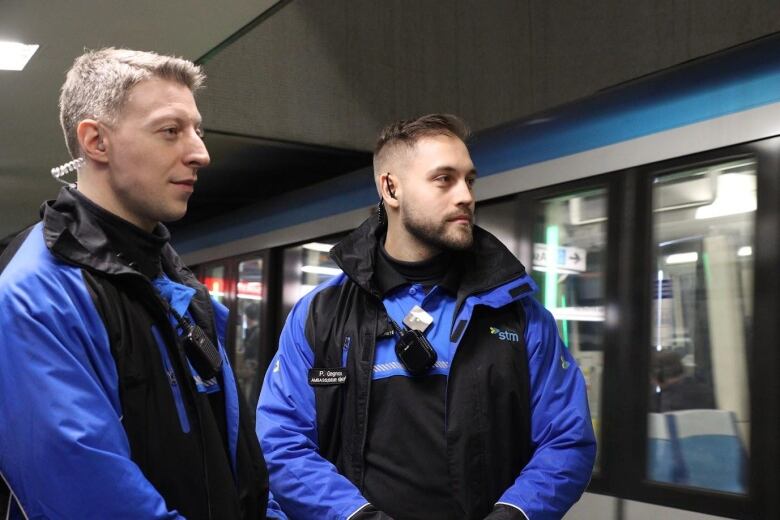 Two men stand in front of a metro train.