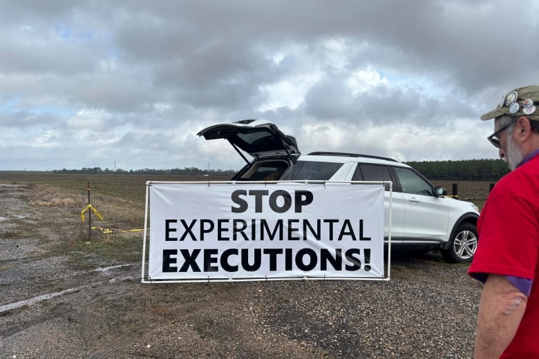 A man with his back turned looks toward a sign in front of a parked car. The sign reads, 