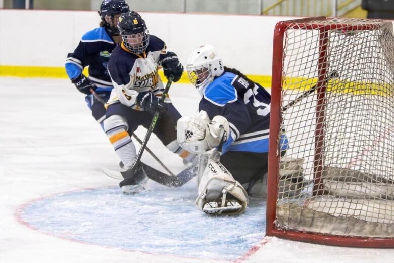 Girl hockey players competing in front of the net. 