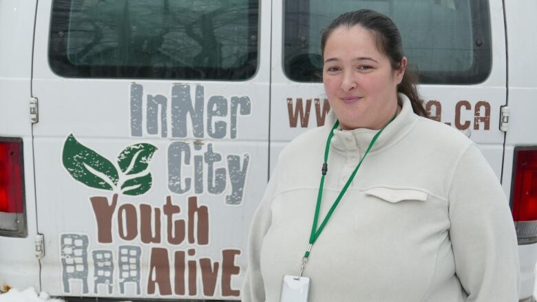 A woman in a white sweater standing outside next to a van. 