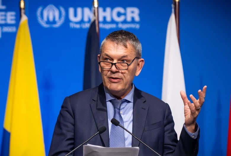 A man in a suit wearing glasses speaks at a podium.