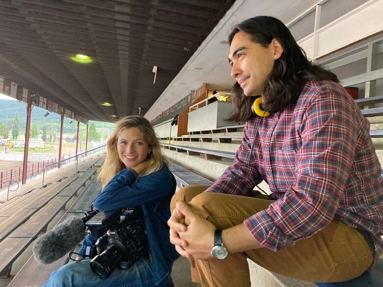 A man and a woman holding a camera sitting in what looks like a stand at a stadium.