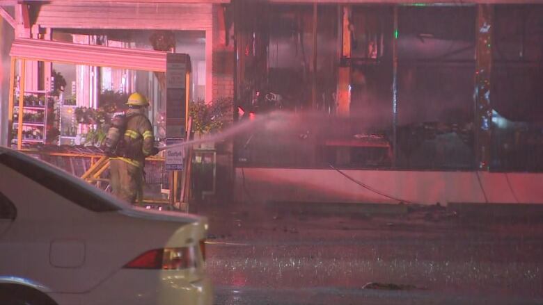 A firefighter sprays water into a building that is burned black.