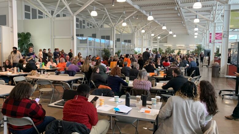 A number of people in a room sitting at tables with foldable chairs.