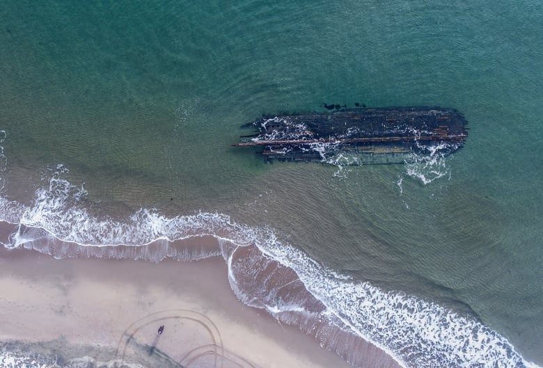 The dark, rotting hull of an old ship lies along the water's edge.