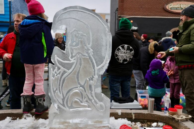 Children marvel at an ice carving of a wolf howling at the moon.