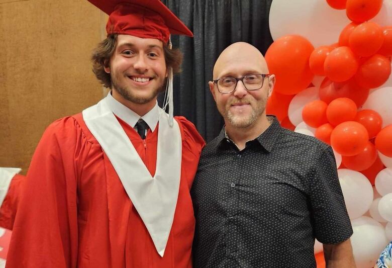 A man stands with his son who is wearing a graduation outfit.