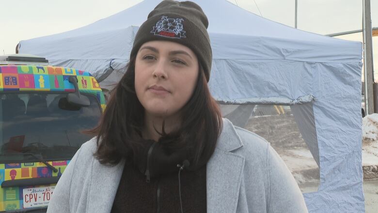 A woman is seen in this close-up shot. She is dressed in a grey jacket, a black sweatshirt, and a dark winter cap.