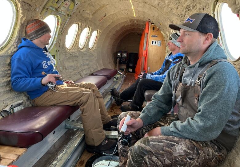 Three men ice fish inside of a decommissioned aircraft.