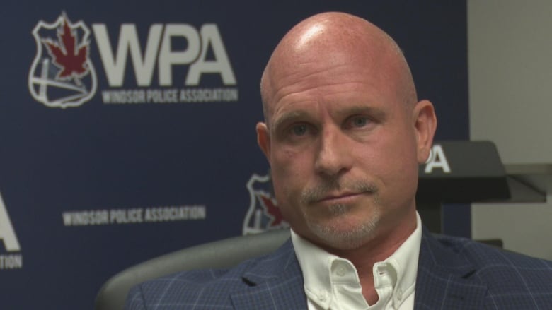 Kent Rice sitting in front of a Windsor Police Association banner