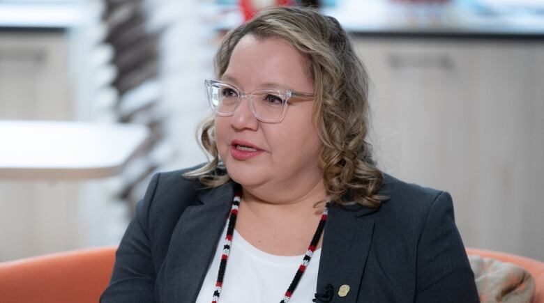 A politician in a suit speaks to a reporter with a beaded medallion with the AFN insignia around her neck.