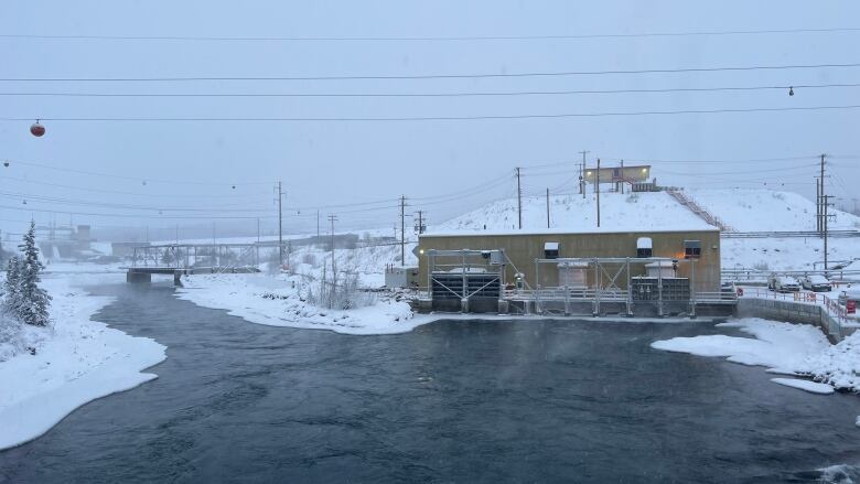 A hydroelectric facility is seen beside a partially-frozen river in winter.