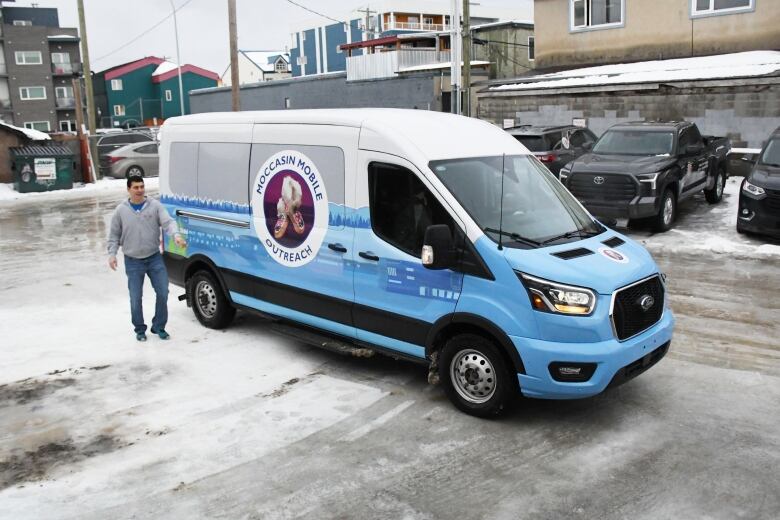 A large blue and white van on an icy street. A man is standing next to it.