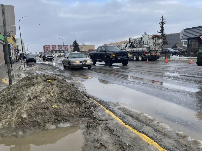 A view of a city street with puddles and dirty snow piled alongside the road.