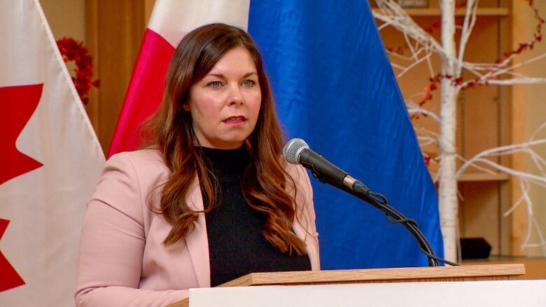 A woman with long, dark hair stands at a podium in front of a microphone. 