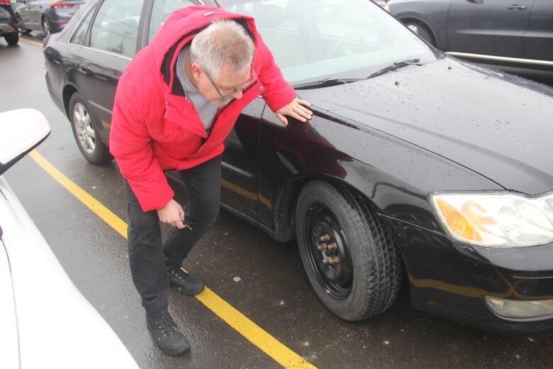 A man in a red jacket looking at a temporary tire installed on his car