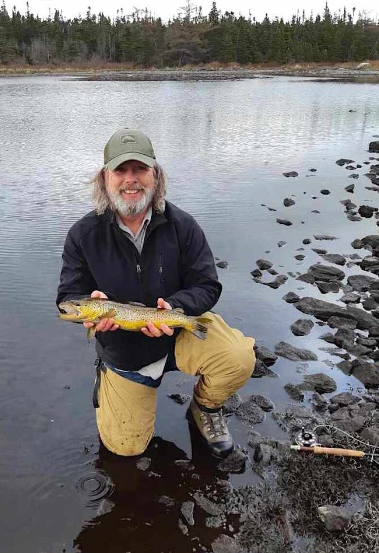 Man kneeling in a body of water, holding a trout.