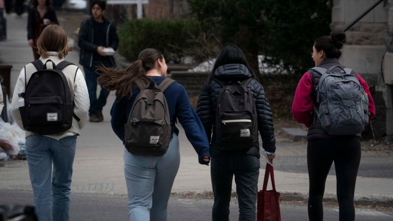 Four students wearing backpacks cross a street. 