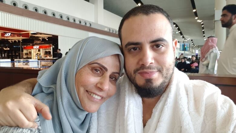 A woman in a blue headscarf poses for a photo of a manin with a beard in a restaurant. 