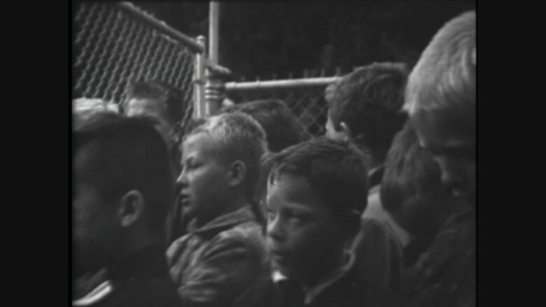 A black-and-white photo of boys behind a fence.