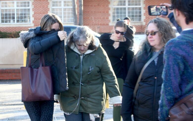 A woman wearing an oxygen tube arrives at court surrounded with a woman shielding her face. 