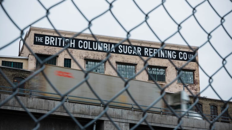 A factory building is seen behind a chain-link fence.