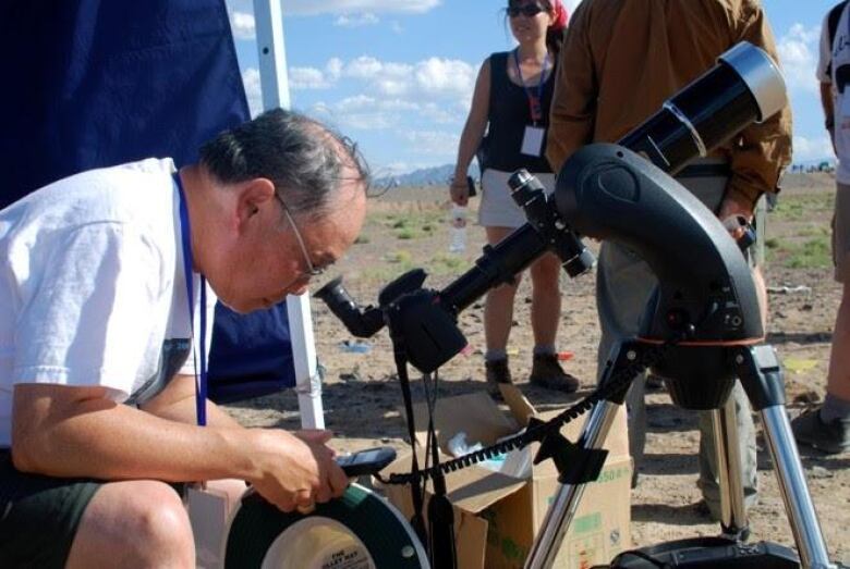 A man looks through a telescope on a sunny day. 