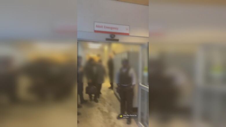 A security guard stands in an emergency department door frame. Their face is blurred.