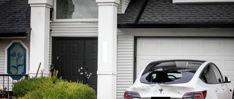 A car with its back windshield shattered is pictured at a single-family home, with white markings on the front door.